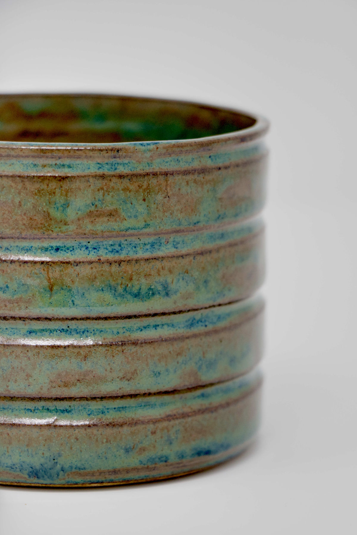 A close-up shot of a blue-green handmade straight-sided vessel.